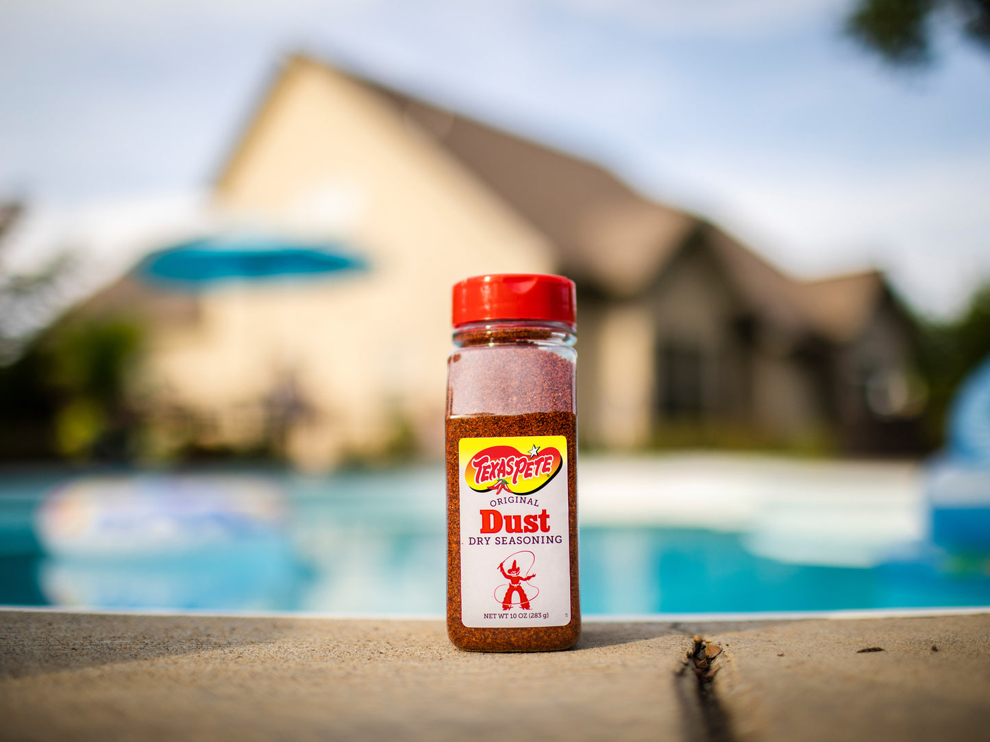 Texas Pete Original Dust Dry Seasoning bottle with a pool and blurred houses in the background