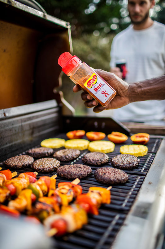 Person grilling burgers and vegetables with a bottle of  Texas Pete Original Dust Dry Seasoning