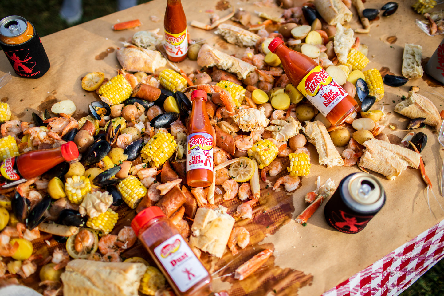 Assorted snacks with Texas Pete sauteed garlic hot sauce bottles on a table with a checkered cloth.