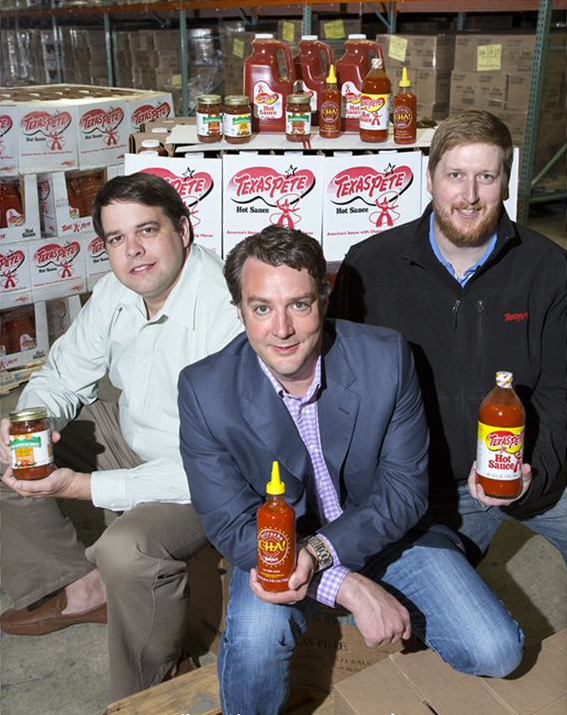 Three men posing with Texas Pete® hot sauce in a warehouse setting