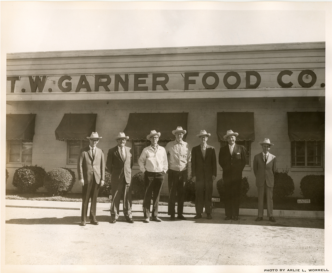 Group of men in suits and hats standing in front of T.W. Garner Food Co.