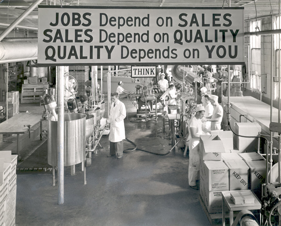 Factory interior with workers and a motivational sign about jobs, sales, and quality.
